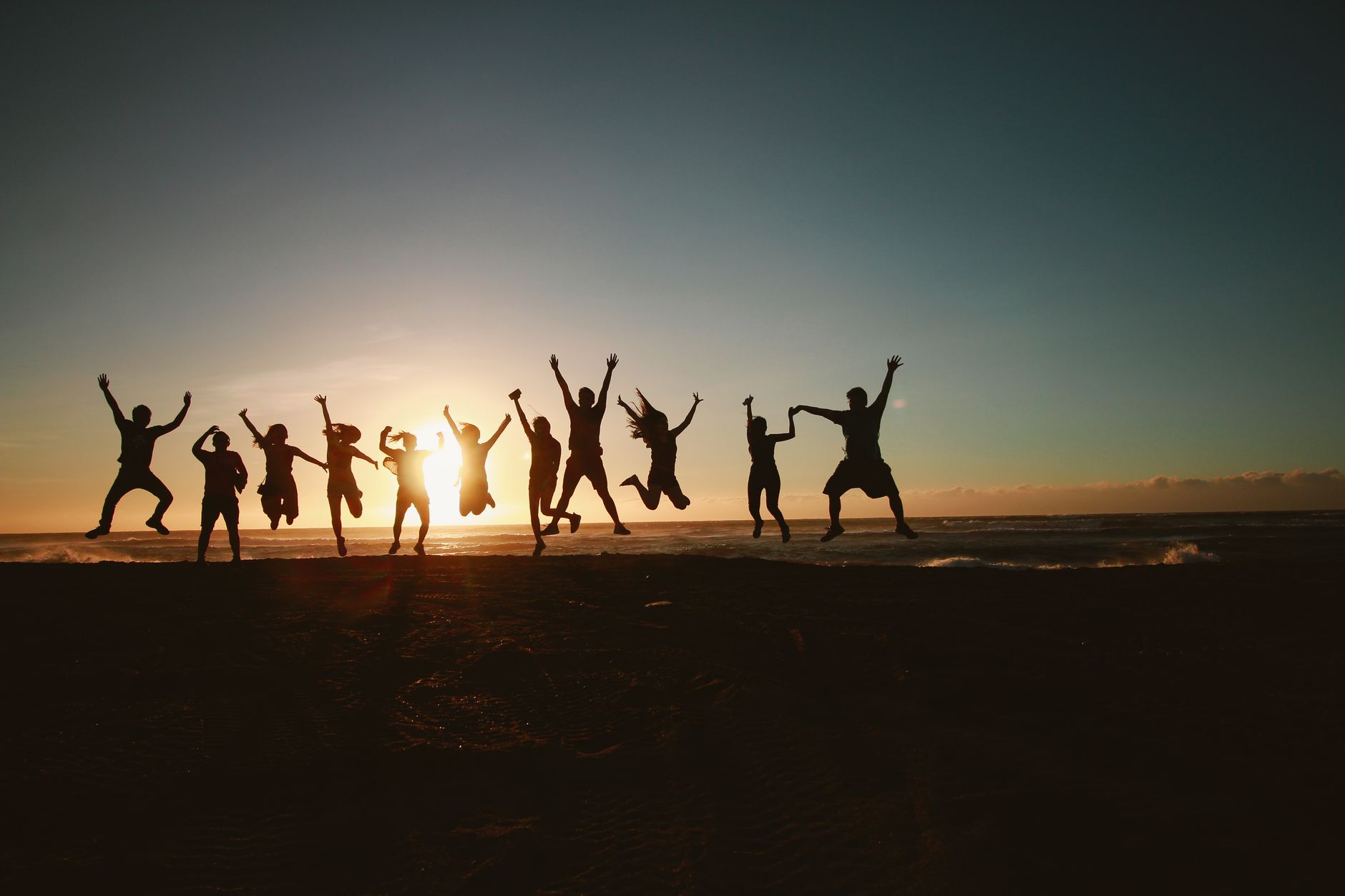 Gruppe springt jubelnd vor einem Sonnenuntergang in die Luft